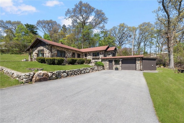 view of front of house featuring a front yard, aphalt driveway, stone siding, and a garage