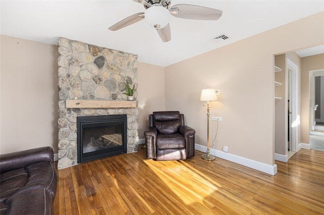 living area with a fireplace, wood-type flooring, a ceiling fan, and visible vents