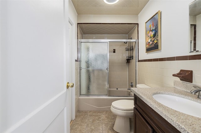 bathroom featuring tile patterned flooring, vanity, toilet, tile walls, and bath / shower combo with glass door