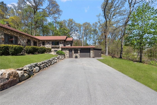 view of front of home featuring an attached garage, a front lawn, stone siding, and aphalt driveway