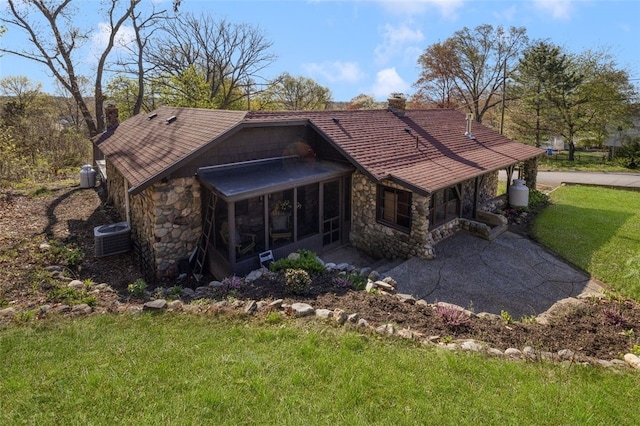 rear view of property featuring a yard, a chimney, a sunroom, and stone siding