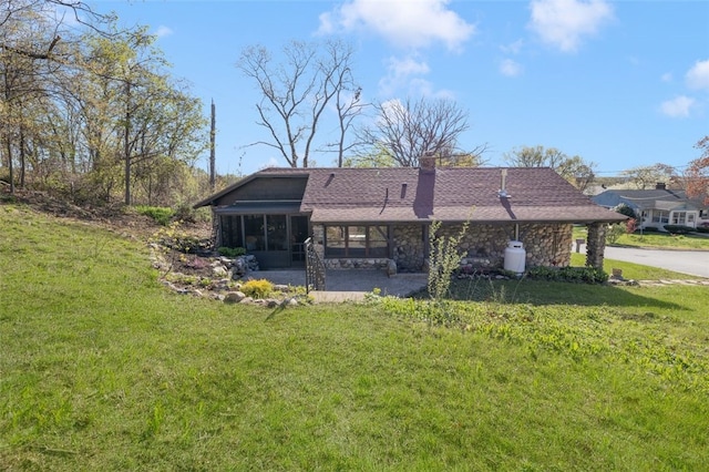 rear view of house featuring a lawn, stone siding, a chimney, and a sunroom