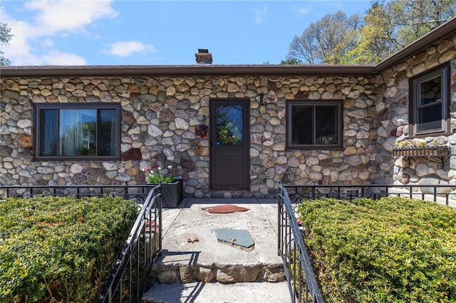 view of exterior entry with fence, a chimney, and stone siding