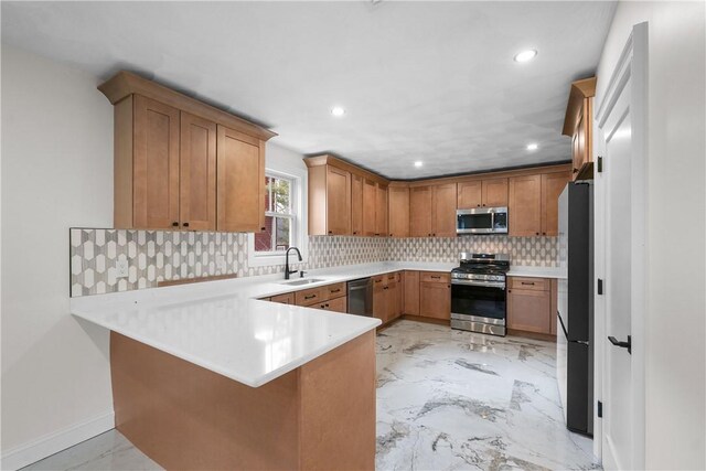 kitchen with backsplash, a sink, light countertops, a peninsula, and stainless steel appliances
