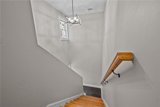 stairs with baseboards, an inviting chandelier, wood finished floors, and visible vents