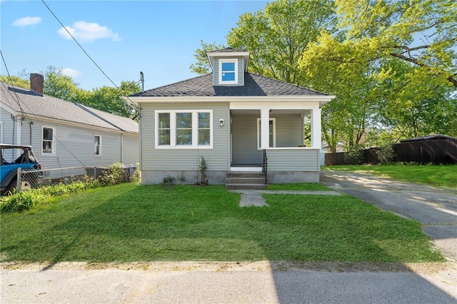 bungalow-style house featuring fence, covered porch, roof with shingles, and a front yard