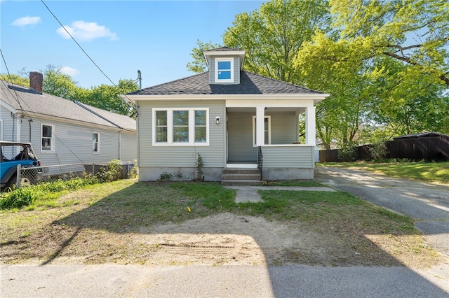 bungalow featuring covered porch, fence, and a shingled roof