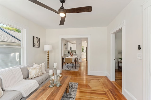 living room featuring a ceiling fan, baseboards, and light wood-style flooring