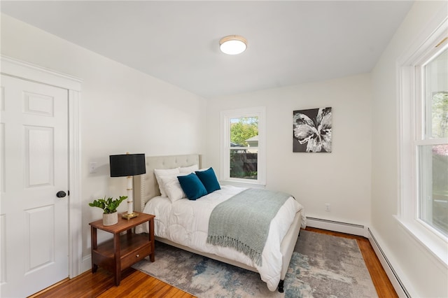 bedroom featuring baseboards, wood finished floors, and a baseboard radiator