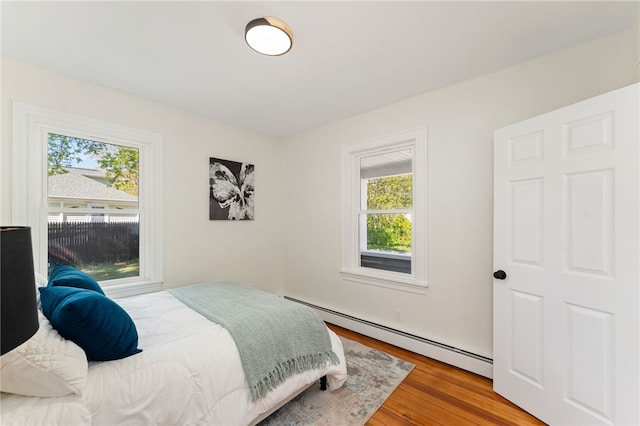 bedroom with multiple windows, baseboard heating, and wood finished floors