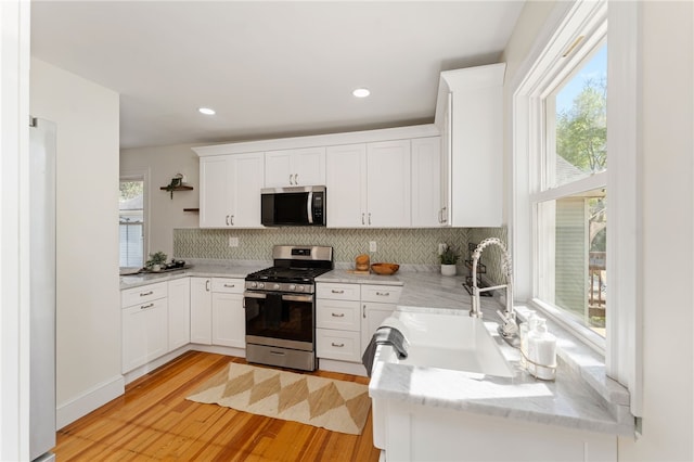 kitchen with a sink, stainless steel appliances, light wood finished floors, and a healthy amount of sunlight
