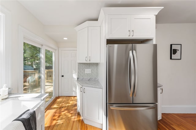 kitchen with freestanding refrigerator, decorative backsplash, baseboards, white cabinetry, and light wood-style flooring