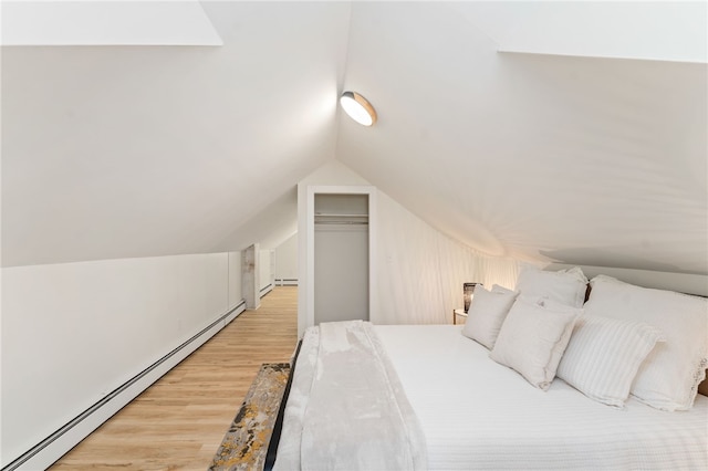 bedroom featuring a closet, a baseboard radiator, vaulted ceiling, and wood finished floors