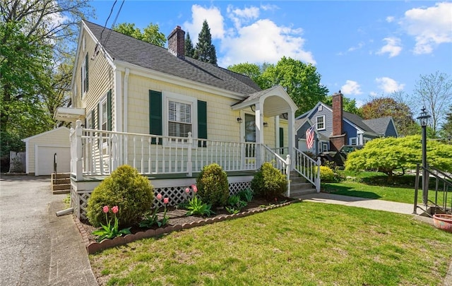 bungalow with covered porch, a chimney, roof with shingles, an outbuilding, and a front lawn