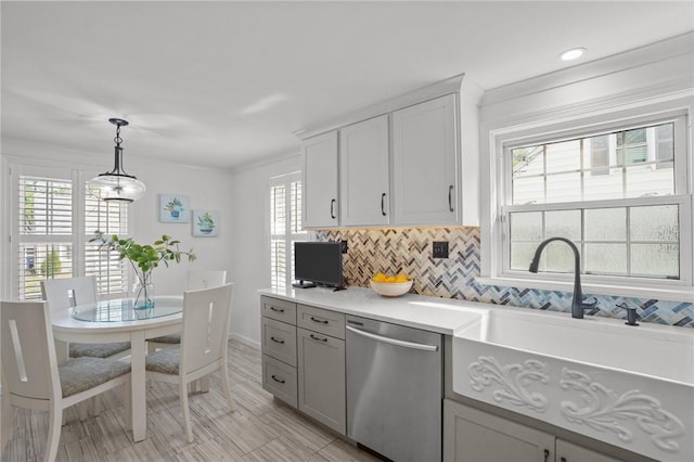 kitchen featuring stainless steel dishwasher, light countertops, a sink, backsplash, and decorative light fixtures