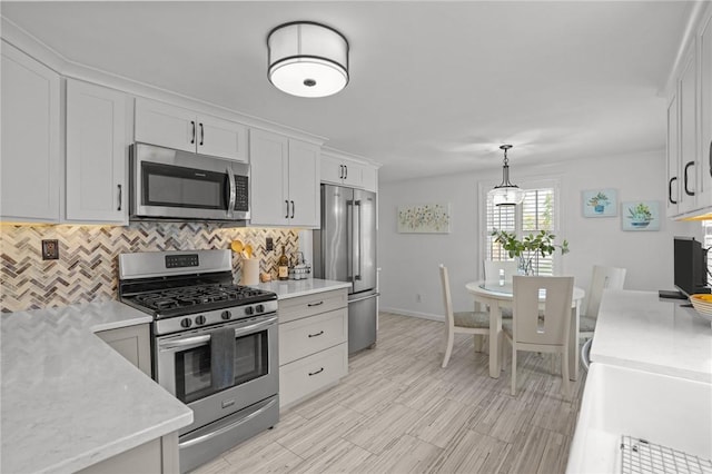 kitchen with white cabinets, stainless steel appliances, baseboards, decorative light fixtures, and tasteful backsplash