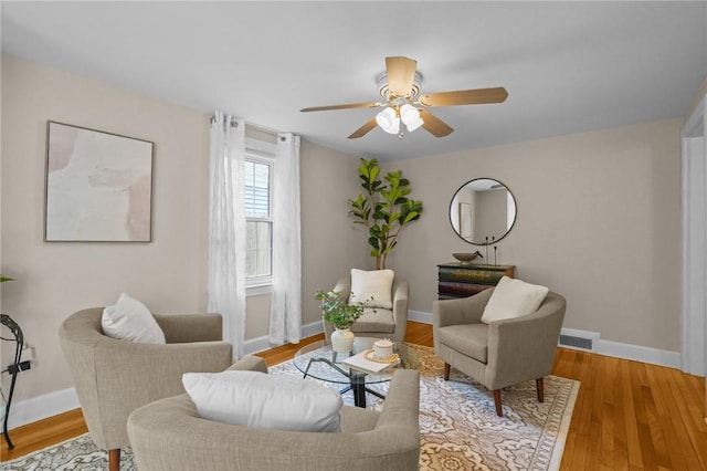 living area with a ceiling fan, baseboards, visible vents, and wood finished floors