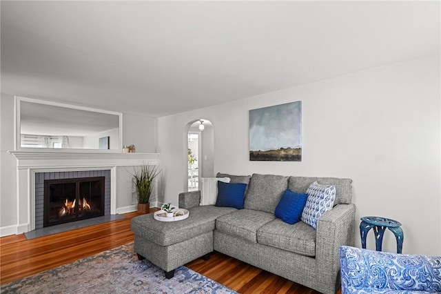 living room with a brick fireplace, arched walkways, and wood finished floors