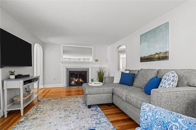 living room featuring arched walkways, a brick fireplace, and wood finished floors