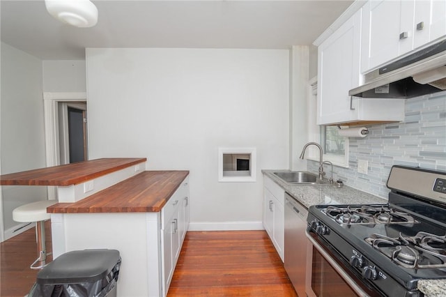 kitchen with appliances with stainless steel finishes, a sink, wooden counters, baseboards, and under cabinet range hood