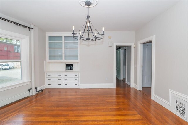 unfurnished dining area with baseboards, an inviting chandelier, wood finished floors, and visible vents