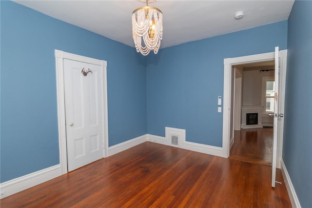 empty room with an inviting chandelier, baseboards, wood finished floors, and visible vents