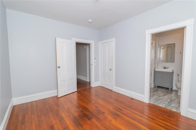 unfurnished bedroom featuring baseboards, ensuite bath, wood finished floors, and a closet