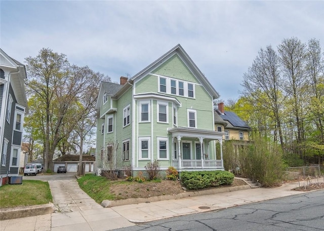 view of front of house featuring central air condition unit, a detached garage, a chimney, and a porch