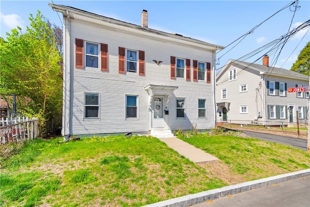 colonial-style house featuring fence, a chimney, and a front lawn
