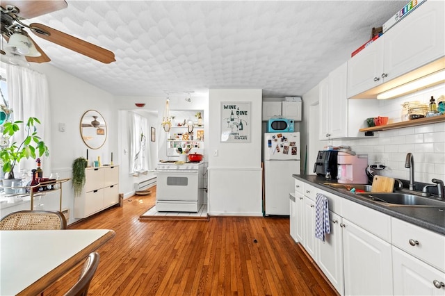 kitchen with dark countertops, a baseboard radiator, a sink, white appliances, and tasteful backsplash