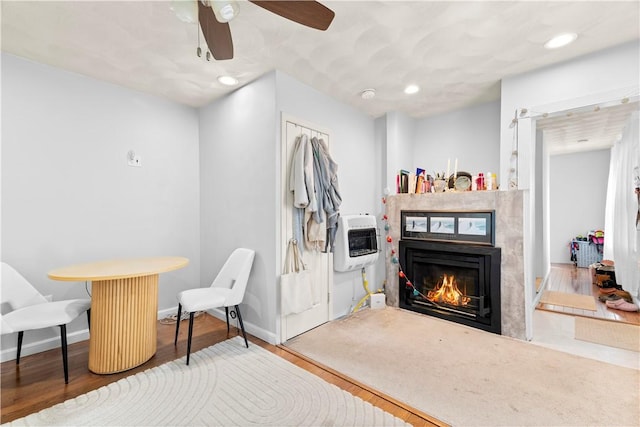 living area with a warm lit fireplace, baseboards, heating unit, and wood finished floors