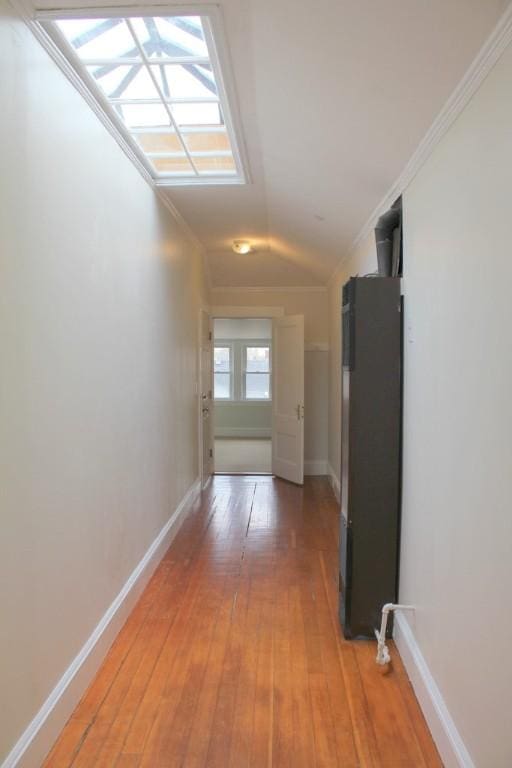 hall with baseboards, ornamental molding, light wood-style flooring, and vaulted ceiling with skylight