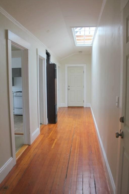 hall featuring baseboards, light wood-style flooring, crown molding, and vaulted ceiling