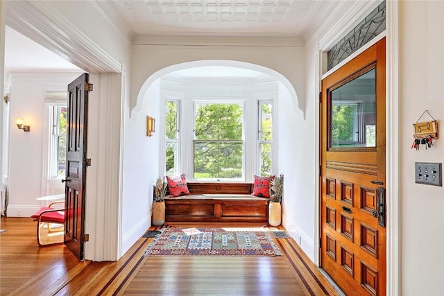 corridor featuring baseboards, arched walkways, wood finished floors, and a healthy amount of sunlight