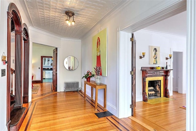corridor with decorative columns, ornamental molding, radiator, and light wood-style floors