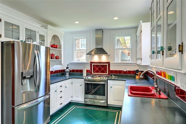 kitchen featuring wall chimney range hood, appliances with stainless steel finishes, dark countertops, a sink, and white cabinetry