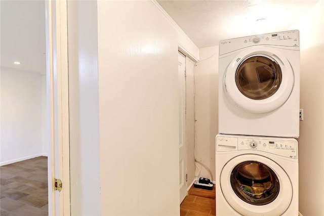 washroom featuring stacked washer and dryer, baseboards, wood finished floors, and laundry area