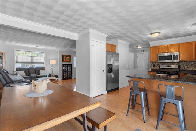 kitchen featuring a breakfast bar area, backsplash, appliances with stainless steel finishes, brown cabinets, and light wood-style flooring