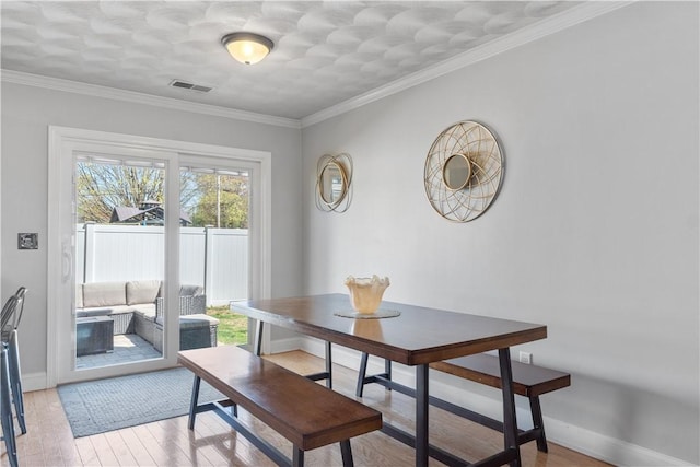 dining room featuring light wood-style floors, baseboards, ornamental molding, and visible vents