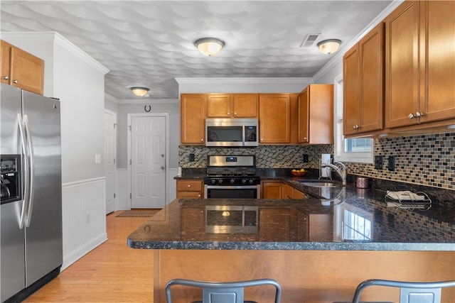kitchen with a sink, brown cabinetry, light wood-style flooring, dark stone counters, and stainless steel appliances