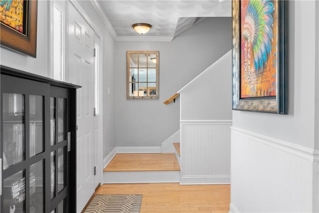 entrance foyer with stairs, crown molding, wood finished floors, and a wainscoted wall