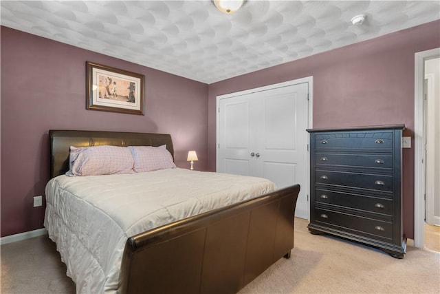bedroom with baseboards, a closet, and light colored carpet