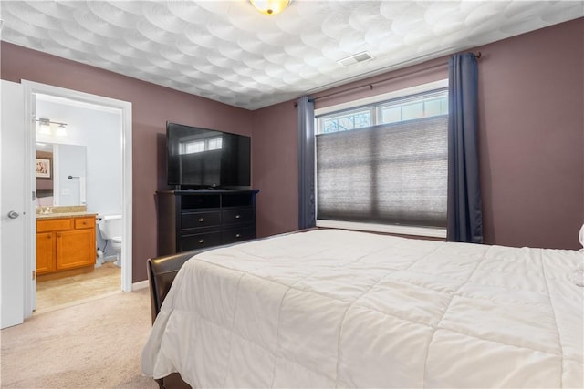 bedroom with visible vents, ensuite bathroom, and light carpet