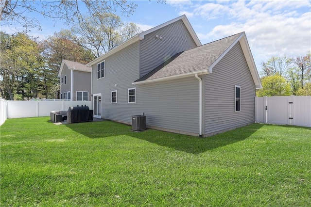 rear view of property with a lawn, a gate, a fenced backyard, and a shingled roof