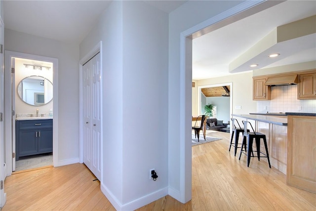 hallway featuring light wood-style floors, baseboards, and a sink
