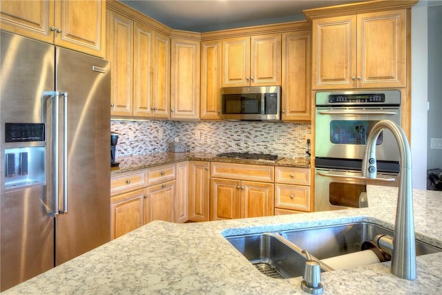 kitchen featuring a sink, appliances with stainless steel finishes, backsplash, and light stone countertops