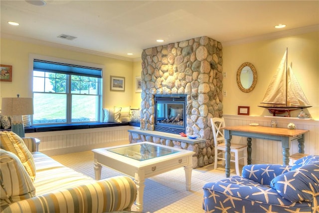 living room with ornamental molding, wainscoting, a stone fireplace, and visible vents