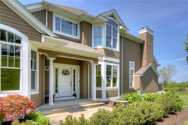 property entrance with a chimney and a shingled roof