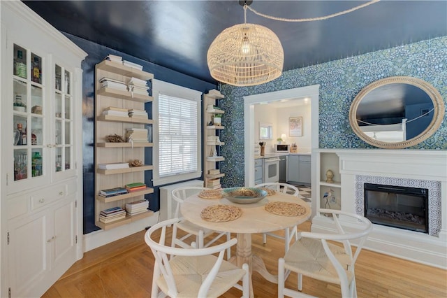 dining room with light wood-style flooring, wallpapered walls, and a tile fireplace