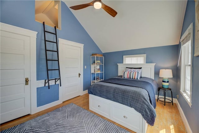 bedroom featuring a ceiling fan, vaulted ceiling, multiple windows, and light wood-style flooring